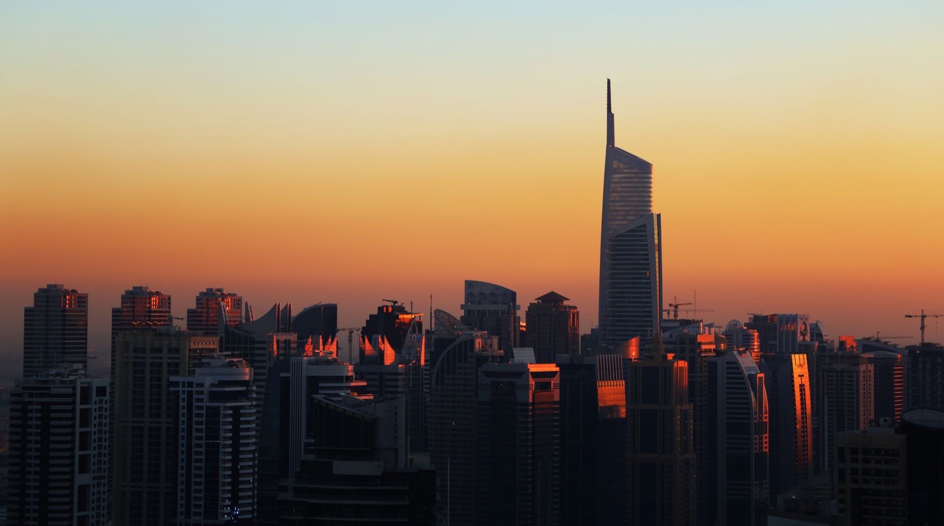 Strassenzug in Al Satwa in der Abenddaemmerung, niedrige Bestandsgebaeude im Vordergrund, dahinter die beleuchtete Skyline entlang der Sheikh Zayed Road
