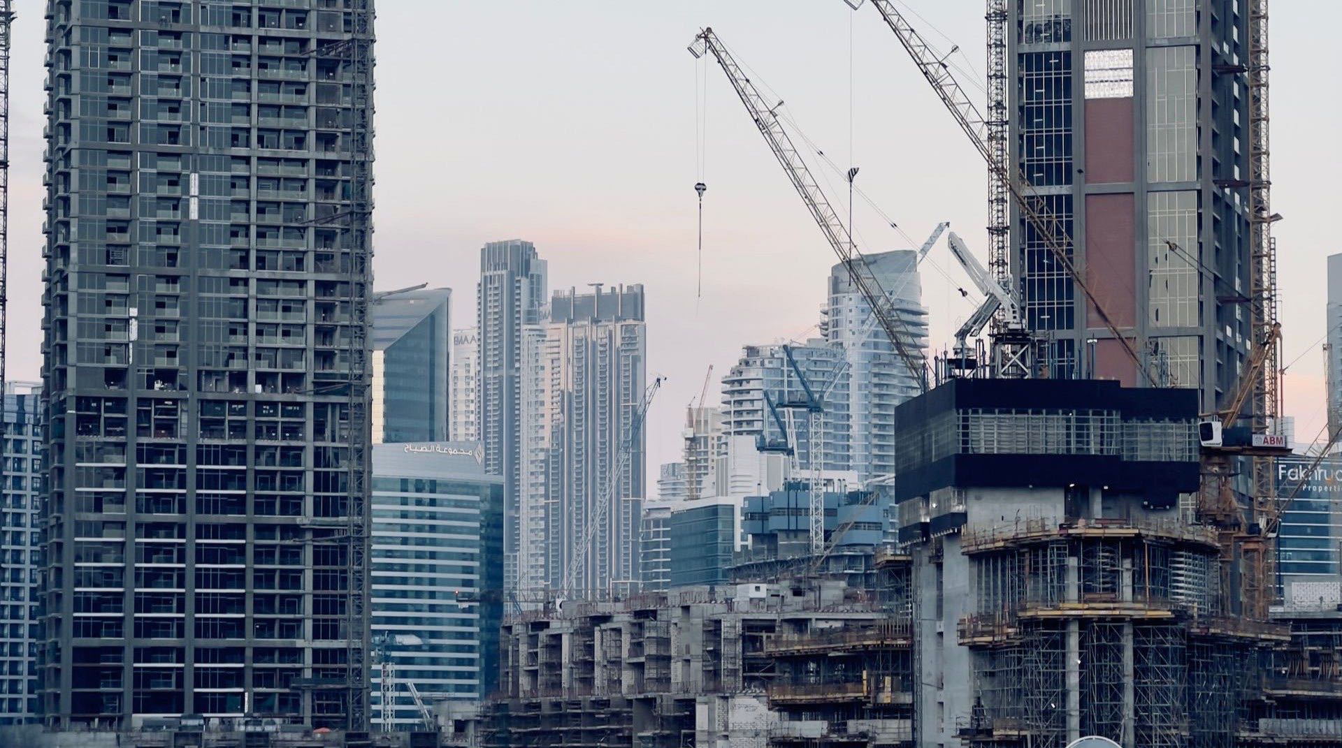 Moderne Apartmenthochhäuser im Stadtteil Arjan in Dubai bei Abenddämmerung, davor begrünte Boulevards und im Hintergrund die weite Wohnbebauung von Dubailand