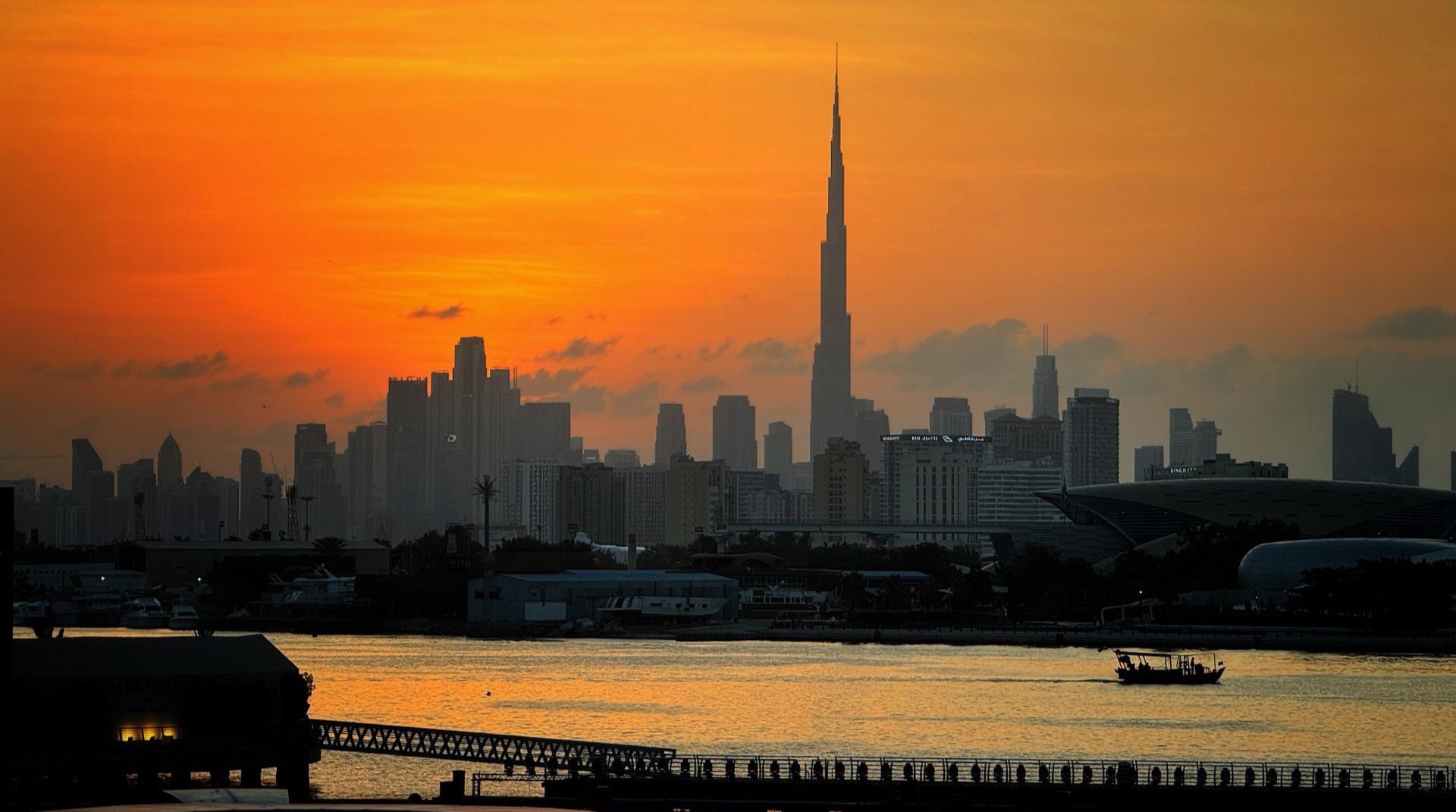 Niedrige Apartmentgebaeude von Dubai Motor City in der Abenddaemmerung, dahinter die weite Stadtsilhouette und Hauptverkehrsachsen