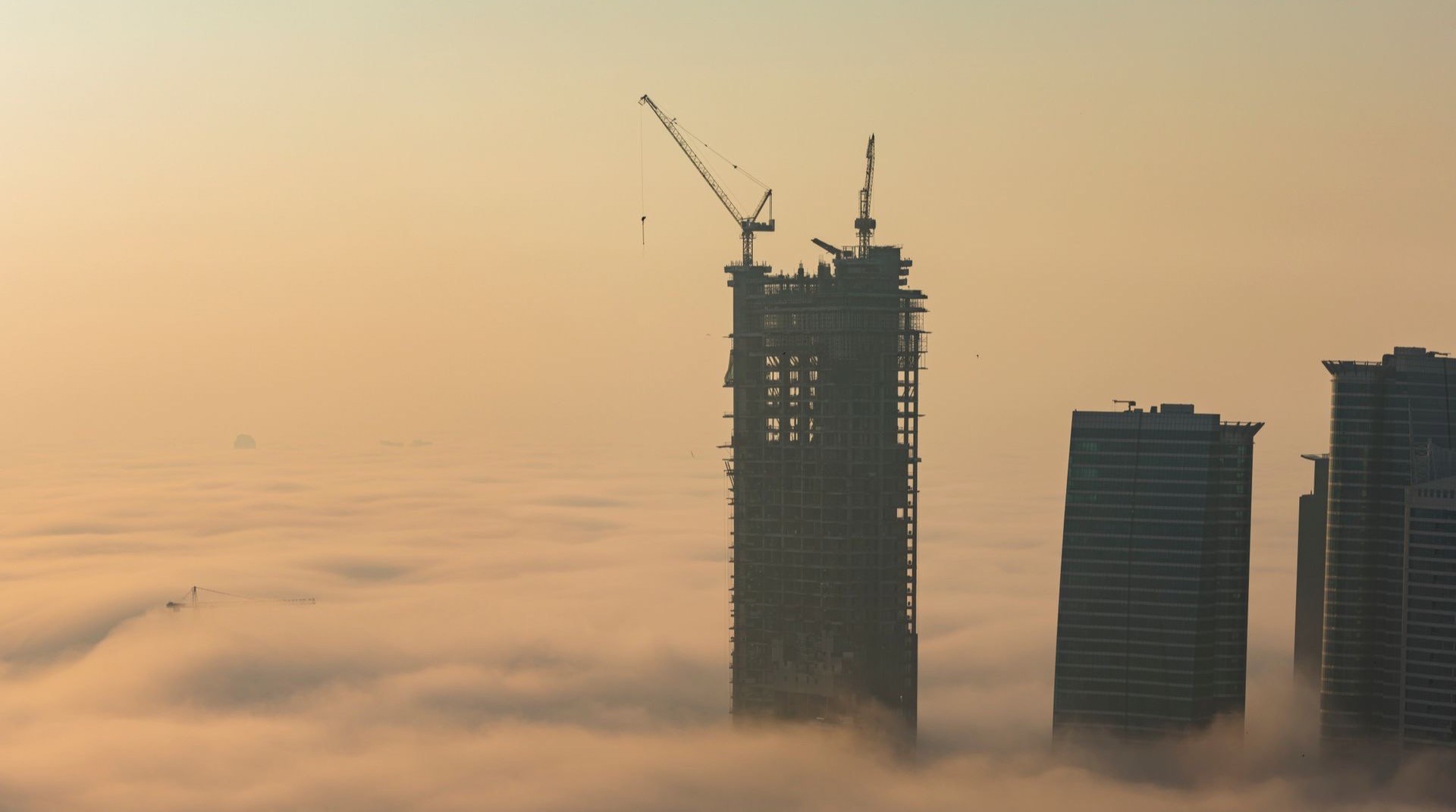 Off-Plan-Apartmenttuerme in Majan, Dubailand, bei Abenddaemmerung mit weiten Hauptverkehrsachsen und offener Bauflaeche im Hintergrund