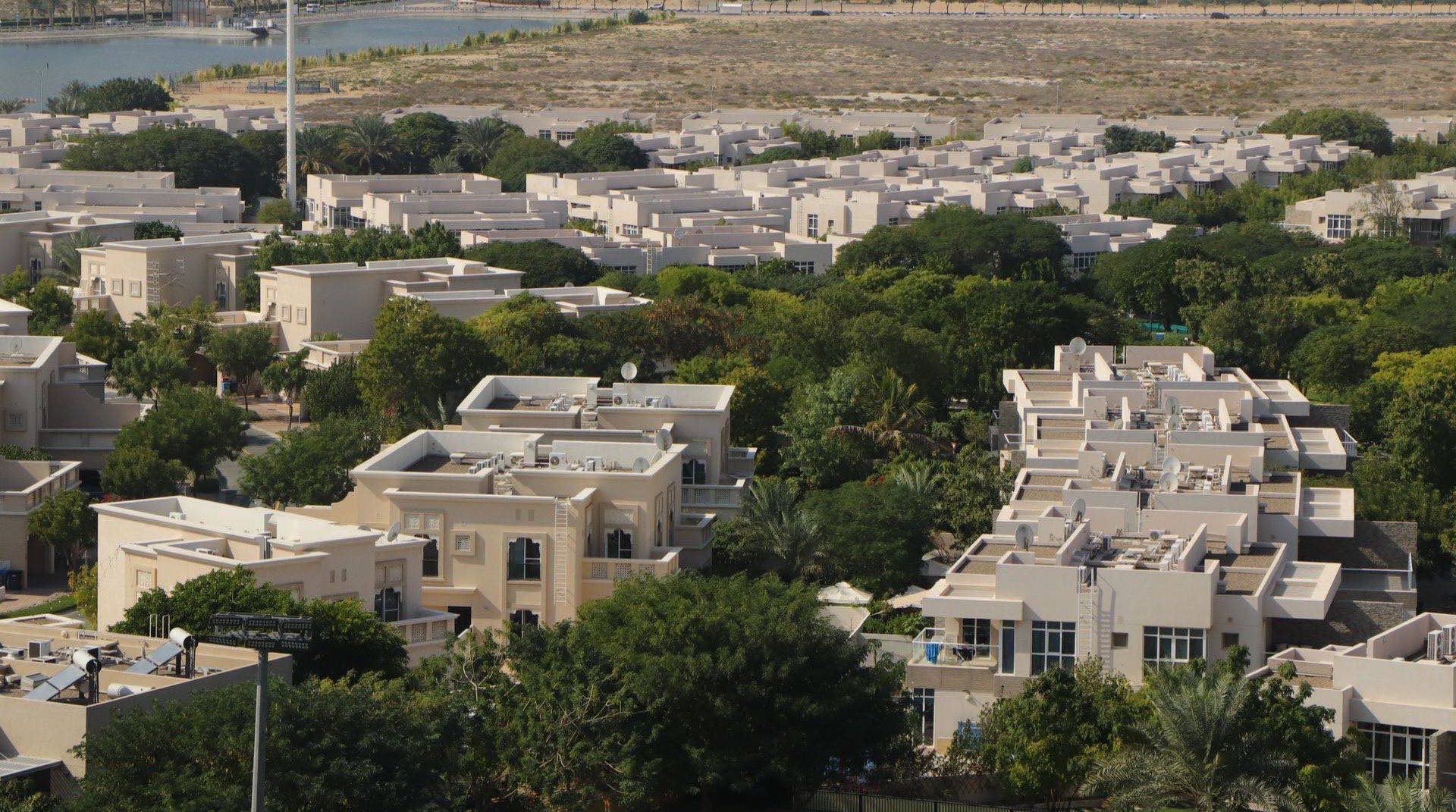 Blick über die Town-Square-Community in Dubai bei Abenddämmerung, mit dem zentralen Park, niedrigen Apartmentgebäuden und Townhouse-Reihen unter warmem Himmel
